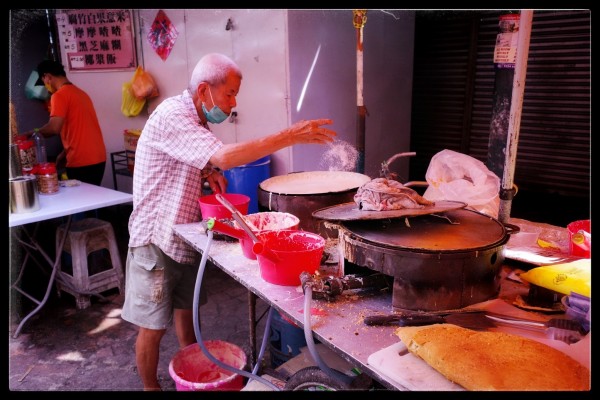 A man throws a handful of rice into a pot on a crowded cooking station