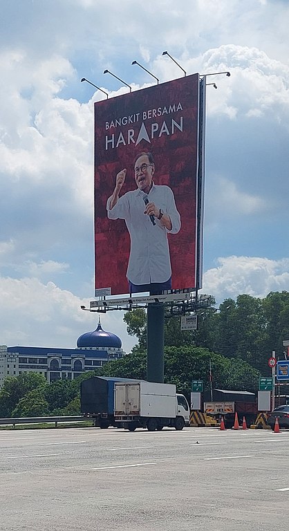A large political poster on the roadside showing a man giving a speech