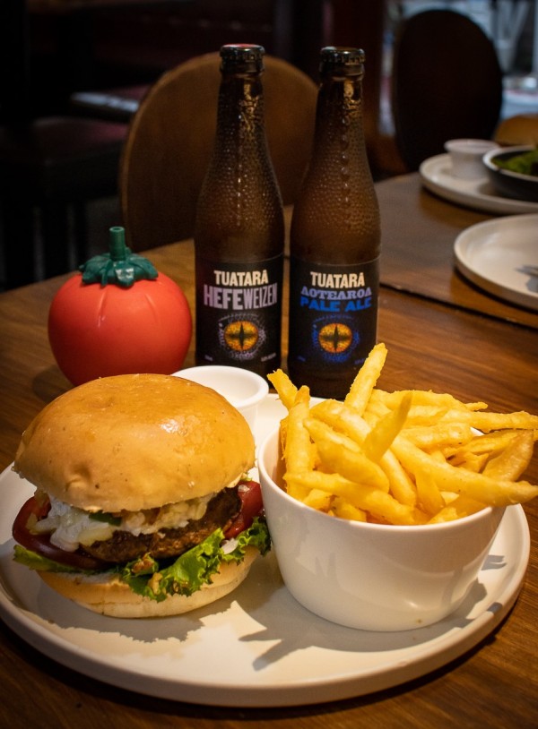 A burger and fries sit in front of two bottles of Tuatara beer and a tomato sauce bottle.